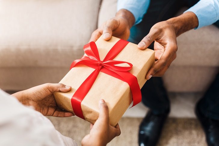 one person gives another a gift box with a red bow